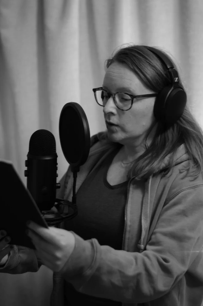 A black and white photograph of Amy Louise recording in front of a microphone in her studio.